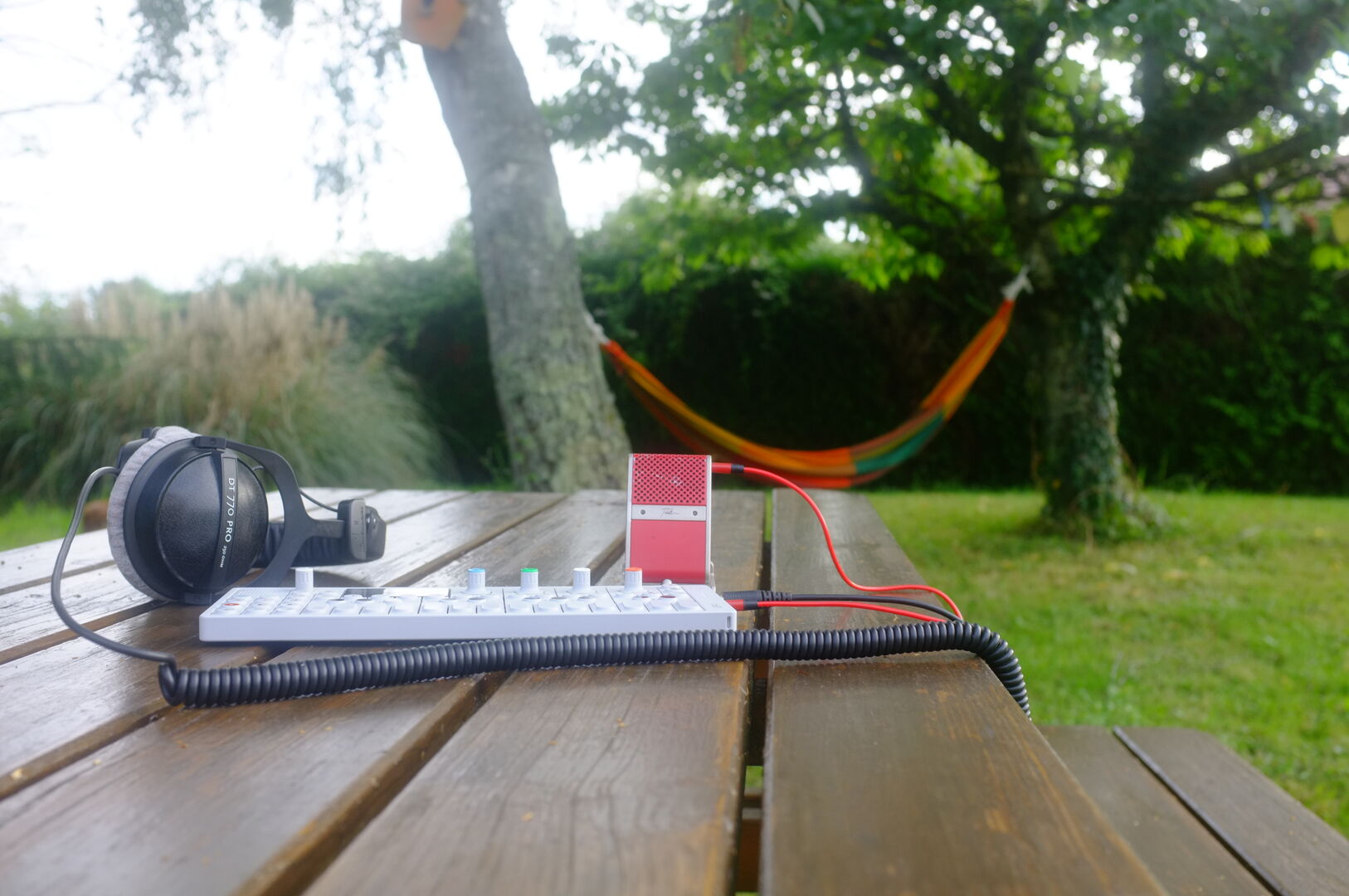 a synth, a microphone and headphone on a wooden table in a garden